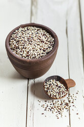 Earthenware dish and wooden spoon of organic quinoa, Chenopodium quinoa, on white wood - SBDF001159