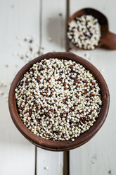 Earthenware dish and wooden spoon of organic quinoa, Chenopodium quinoa, on white wood - SBDF001161