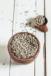 Earthenware dish and wooden spoon of organic hemp seed, Cannabis sativa, on white wood - SBDF001168