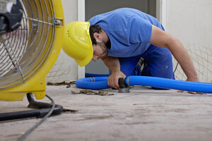 Worker fixing hose of dehumidifier in an apartment which is damaged by flooding - LAF001027