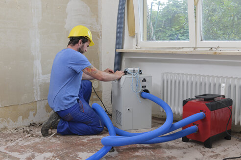 Worker adjusting dehumidifier in an apartment which is damaged by flooding - LAF001030