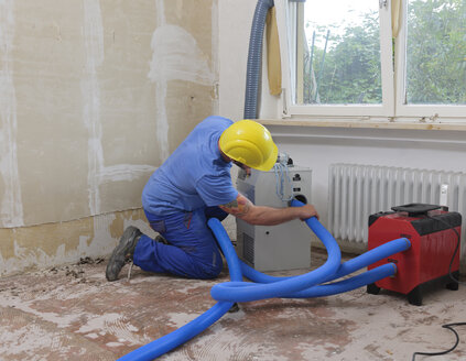 Arbeiter, der den Schlauch eines Luftentfeuchters in einer durch Überschwemmung beschädigten Wohnung repariert - LAF001031
