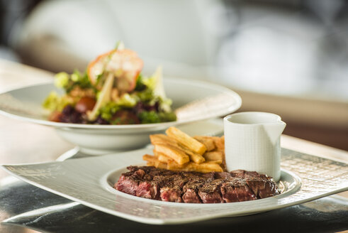 Steak medium rare mit Pommes frites und gemischtem Salat im Hintergrund - KM001340