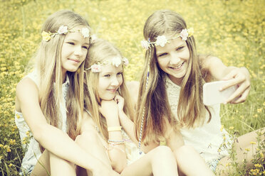 Porträt von drei Mädchen mit Blumenkränzen, die ein Selfie auf einer Blumenwiese machen - GDF000367