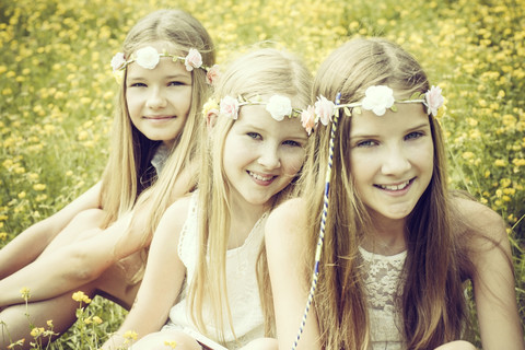 Porträt von drei Mädchen mit Blumenkränzen, die auf einer Blumenwiese sitzen, lizenzfreies Stockfoto