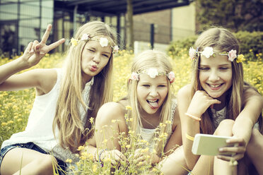 Porträt von drei Mädchen mit Blumenkränzen, die ein Selfie auf einer Blumenwiese machen - GDF000389