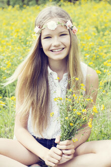 Porträt eines glücklichen Mädchens, das auf einer Blumenwiese sitzt und Blumen trägt - GDF000387