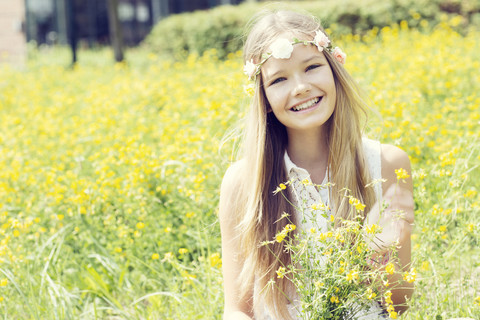 Portrait of a happy girl sitting on a flower meadow wearing flowers stock photo