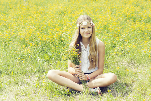 Porträt eines lächelnden Mädchens, das auf einer Blumenwiese sitzt und Blumen trägt - GDF000373