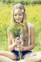 Portrait of a girl sitting on a flower meadow smelling on a bunch of flowers - GDF000368