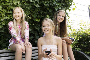 Three smiling girls sitting on a park bench - GDF000369