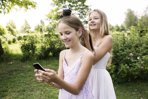 Mädchen benutzt ihr Smartphone, während ihre Schwester ihr Haar bürstet - GDF000385