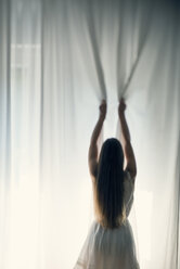 Angry young woman pulling a white curtain, back view - BRF000573