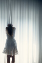 Junge Frau versteckt ihr Gesicht hinter einem weißen Vorhang, Rückenansicht - BRF000575