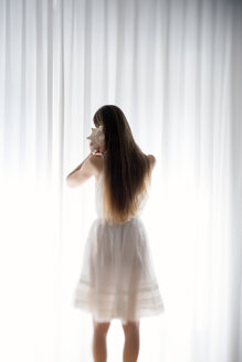 Junge Frau steht mit einer Muschel vor einem weißen Vorhang, Rückansicht - BRF000574