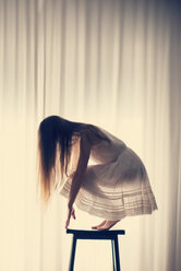 Junge Frau hockt auf einem Hocker vor einem weißen Vorhang, Rückansicht - BRF000581