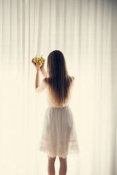 Young woman standing in front of a white curtain holding three pears in her hands, back view - BRF000583