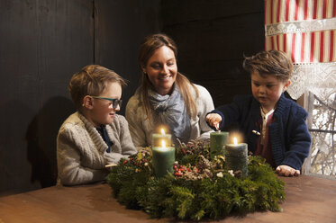 Mutter und ihre beiden kleinen Söhne zünden Kerzen auf einem Adventskranz an - HHF004847