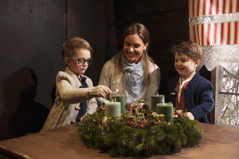 Mutter mit ihren beiden kleinen Söhnen zündet Kerzen auf einem Adventskranz an, lizenzfreies Stockfoto