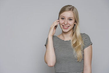 Porträt einer lächelnden jungen Frau, die mit einem Smartphone telefoniert - TCF004110