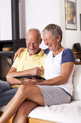 Älteres Paar sitzt auf der Couch und hat Spaß mit einem digitalen Tablet - JUNF000002