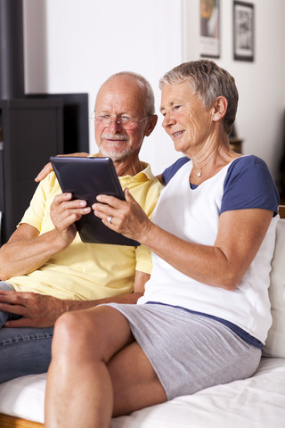 Älteres Paar sitzt auf der Couch und benutzt ein digitales Tablet, lizenzfreies Stockfoto