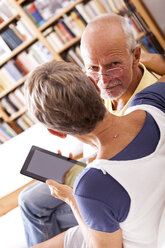 Senior couple sitting on couch using digital tablet - JUNF000004