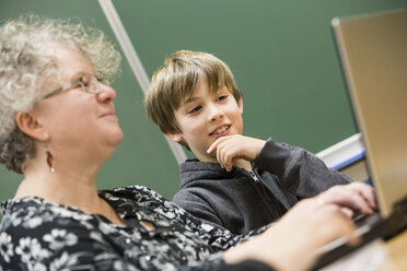 Porträt einer Lehrerin und eines Schülers mit Laptop vor einer Wandtafel - DISF000985