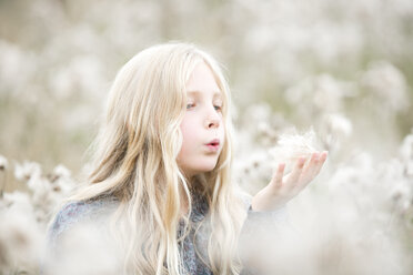 Portrait of girl standing in a field blowing seeds out off her hand - MAEF009021