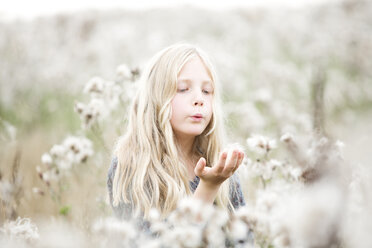 Portrait of girl standing in a field blowing seeds out off her hand - MAEF009023