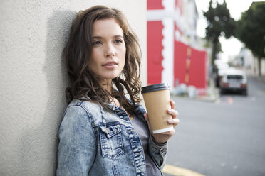 Porträt einer jungen Frau mit Kaffee zum Mitnehmen, die an einer Hausfassade lehnt - ZEF000048