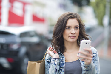 Porträt einer Frau mit Einkaufstasche und Smartphone beim Gehen auf der Straße - ZEF000059