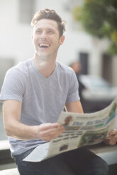 Porträt eines lachenden jungen Mannes mit Zeitung in der Hand - ZEF000074