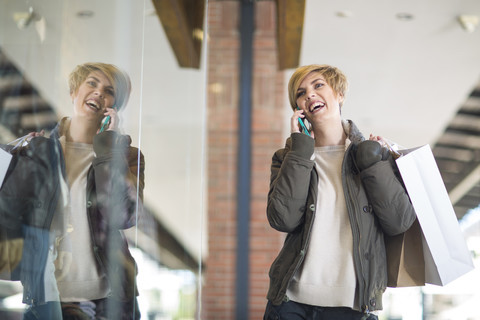 Porträt einer lachenden, telefonierenden Frau vor einem Schaufenster, lizenzfreies Stockfoto