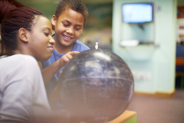 Young woman and boy looking at globe in library - ZEF000191