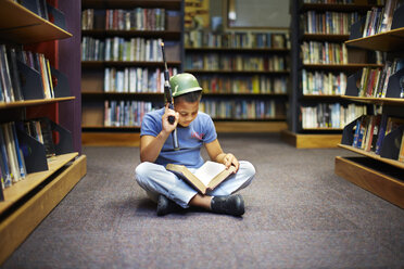 Junge mit Helm und Gewehr beim Lesen eines Buches in einer Bibliothek - ZEF000195