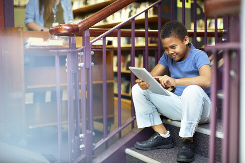 Junge benutzt digitales Tablet in der Bibliothek - ZEF000760