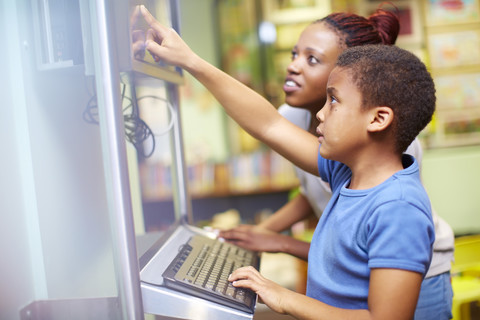 Junge Frau und Junge benutzen Computer in einer Bibliothek, lizenzfreies Stockfoto