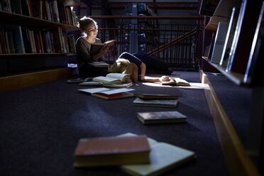 Eine Studentin liegt in einer Bibliothek mit einem Freund auf dem Boden und liest ein Buch - ZEF000120