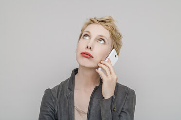 Porträt einer blonden Frau mit Smartphone und Schmollmund, die nach oben schaut - TCF004232