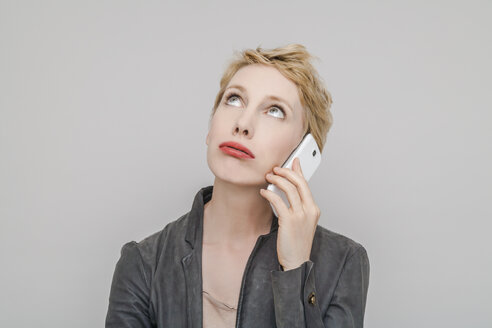 Portrait of blond woman with smartphone pouting mouth looking up - TCF004232