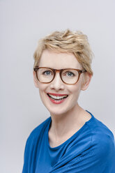 Porträt einer lächelnden blonden Frau mit Brille vor einem grauen Hintergrund - TCF004264