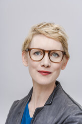 Porträt einer lächelnden blonden Frau mit Brille vor einem grauen Hintergrund - TCF004267