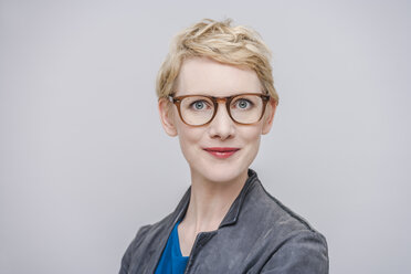 Porträt einer lächelnden blonden Frau mit Brille vor einem grauen Hintergrund - TCF004269