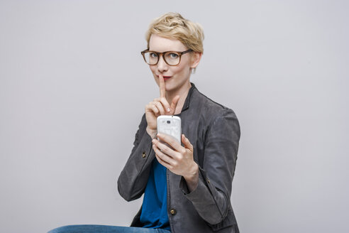Porträt einer blonden Frau mit Finger auf dem Mund vor einem grauen Hintergrund - TCF004272
