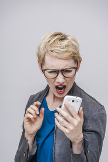 Porträt einer blonden Frau, die auf ihr Smartphone schaut und schreit - TCF004277