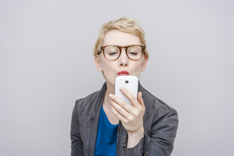 Blonde Frau mit Schmollmund macht ein Selfie mit ihrem Smartphone, lizenzfreies Stockfoto