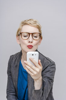 Blonde Frau mit Schmollmund macht ein Selfie mit ihrem Smartphone - TCF004285