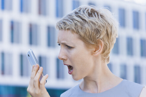 Wütende blonde Frau, die auf ihr Smartphone schreit - TCF004297