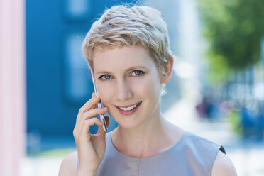 Porträt einer lächelnden blonden Frau, die mit einem Smartphone telefoniert - TCF004305